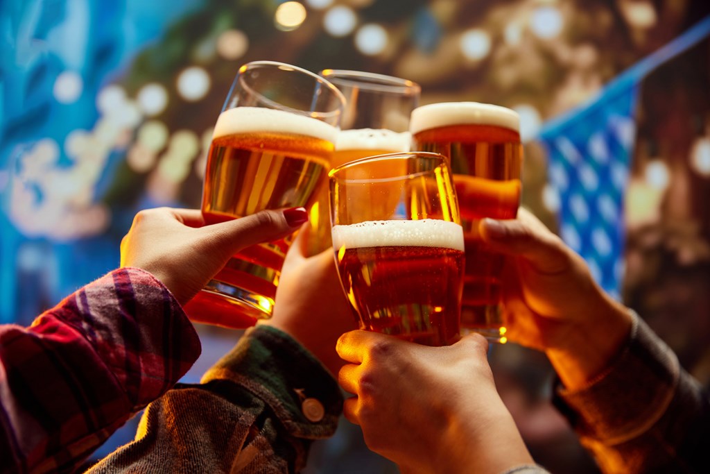 Hands raised in the air with beer glasses in them cheersing at Oktoberfest in a pub