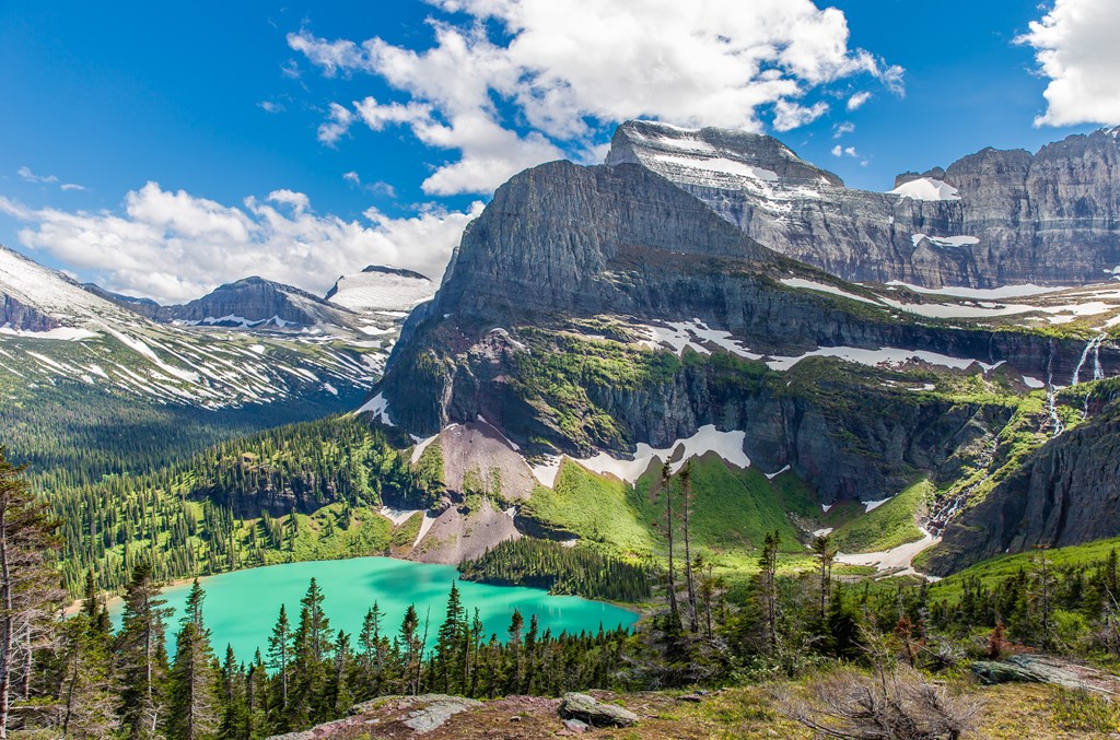 Bright green Grinnell Lake sits at the bottom of small mountain valley in Glacier National Park.