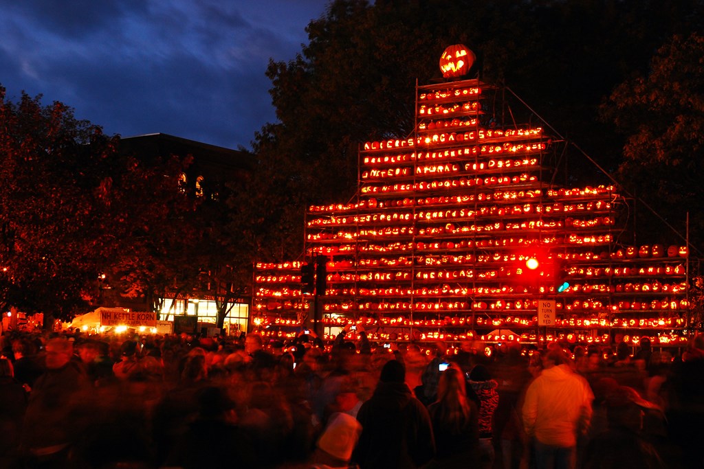 A nighttime view of a crowd in front of a large tower of carved pumpkins at New Hampshire Pumpkin Festival