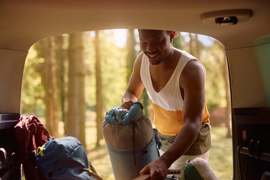 Man packing back of car with camping gear in woods